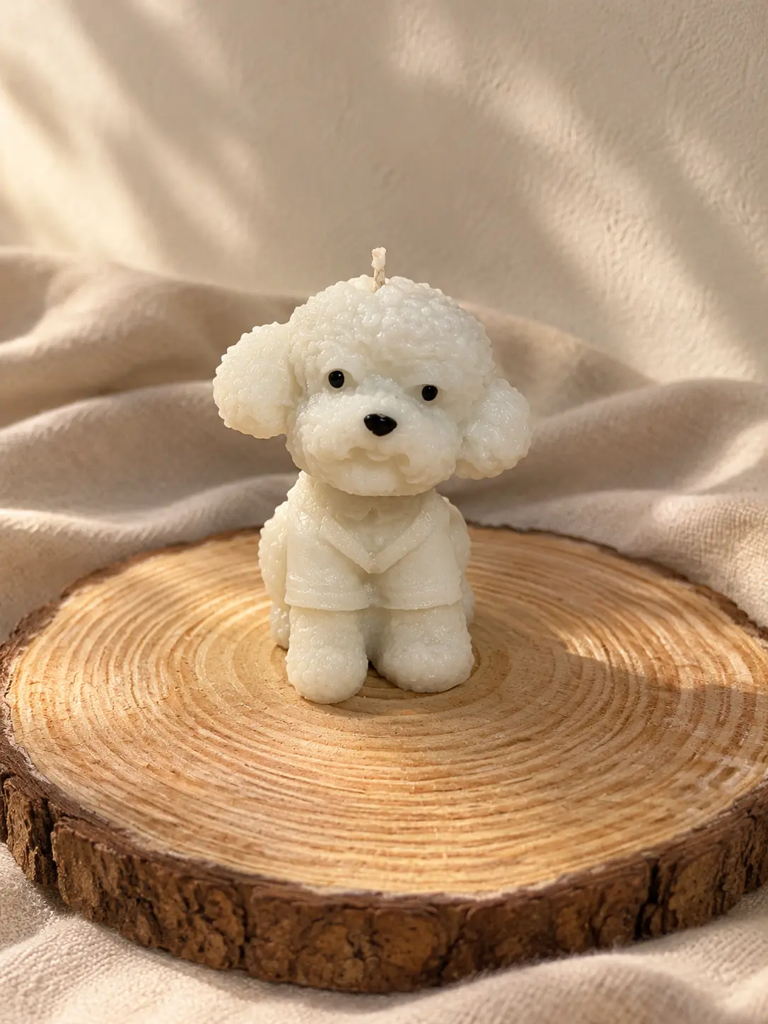 White poodle-shaped candle on a wooden slice
