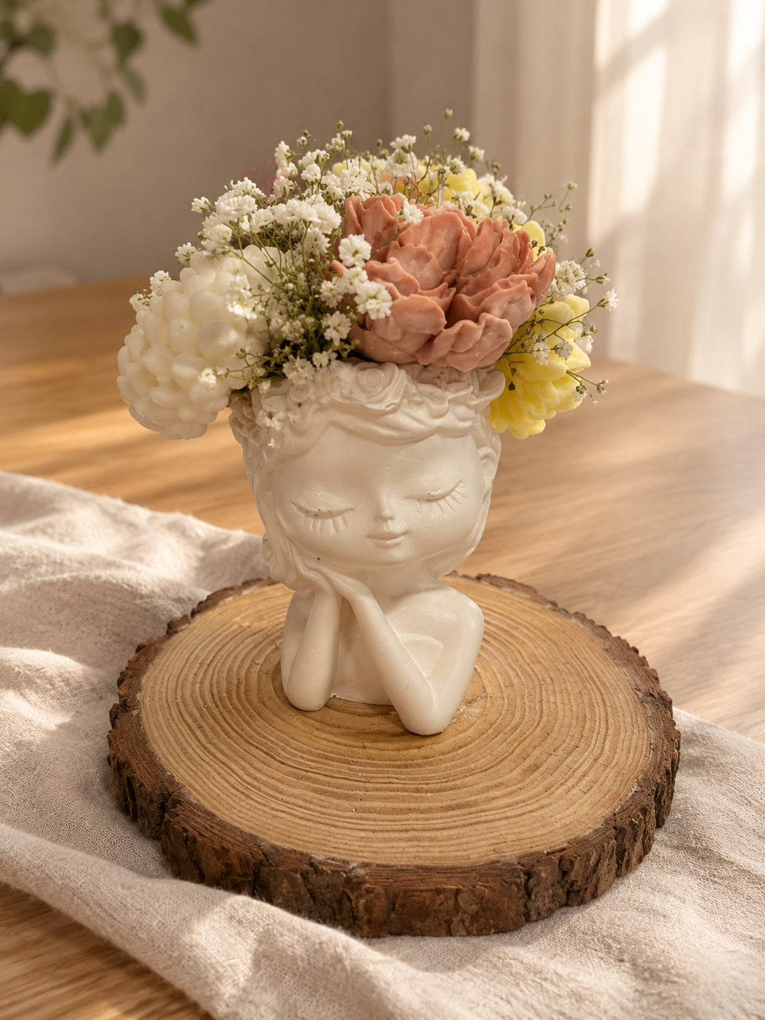 White sculpted face holder filled with pink, yellow and cream wax flowers and baby's breath