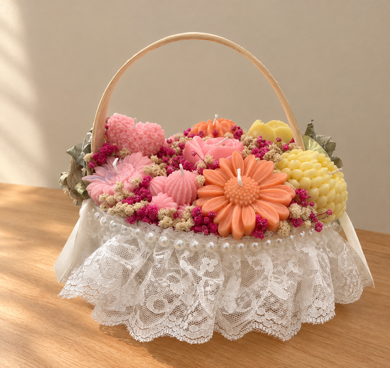 Basket trimmed with white lace and pearls, filled with pink, orange and yellow wax flower and heart candles and dried flowers