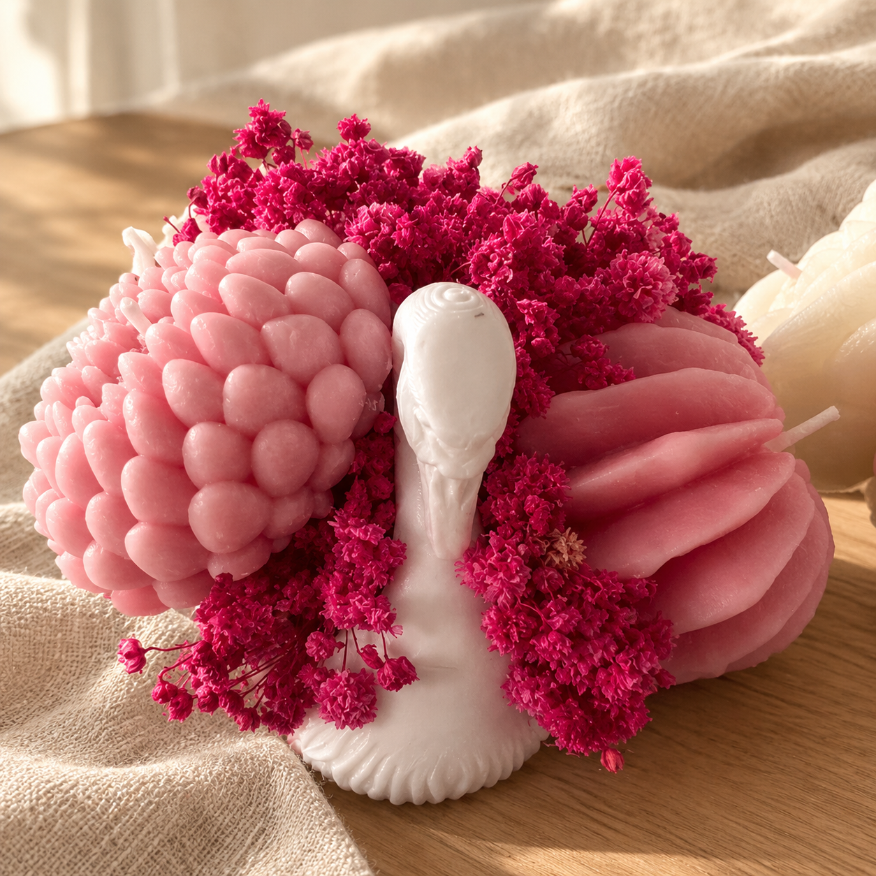 White swan candle surrounded by pink wax wings and bright pink dried flowers
