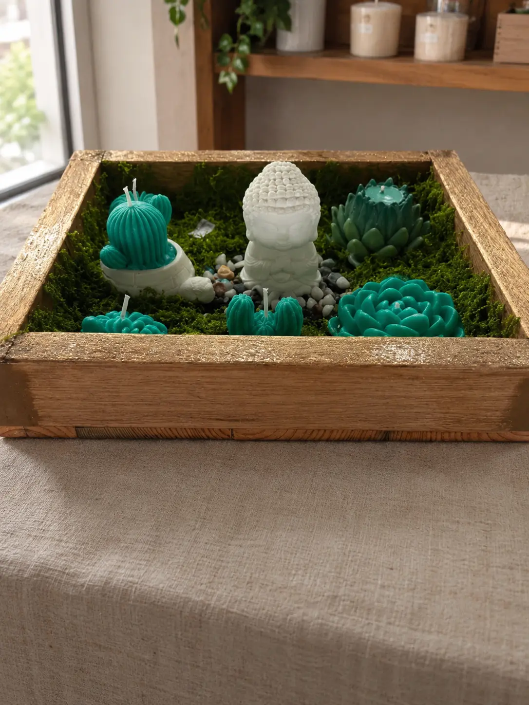 Wooden tray with moss, pebbles, a white Buddha candle and teal cactus and succulent candles