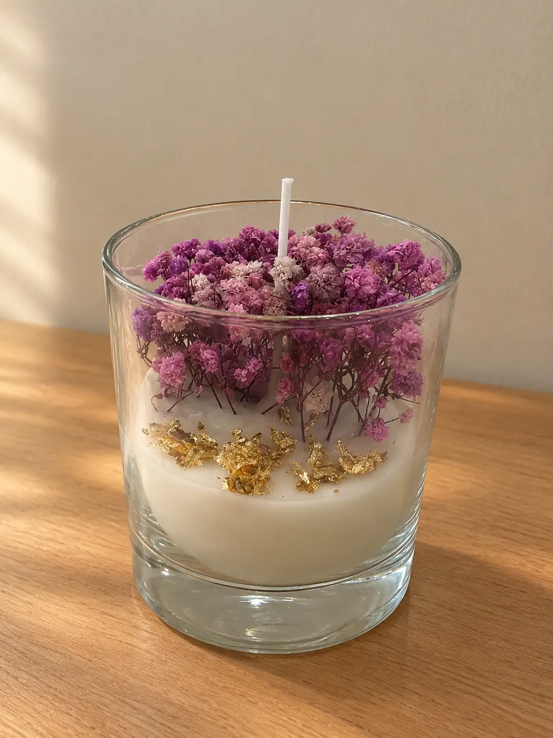 Glass candle of white wax with gold flakes and pink and purple dried gypsophila