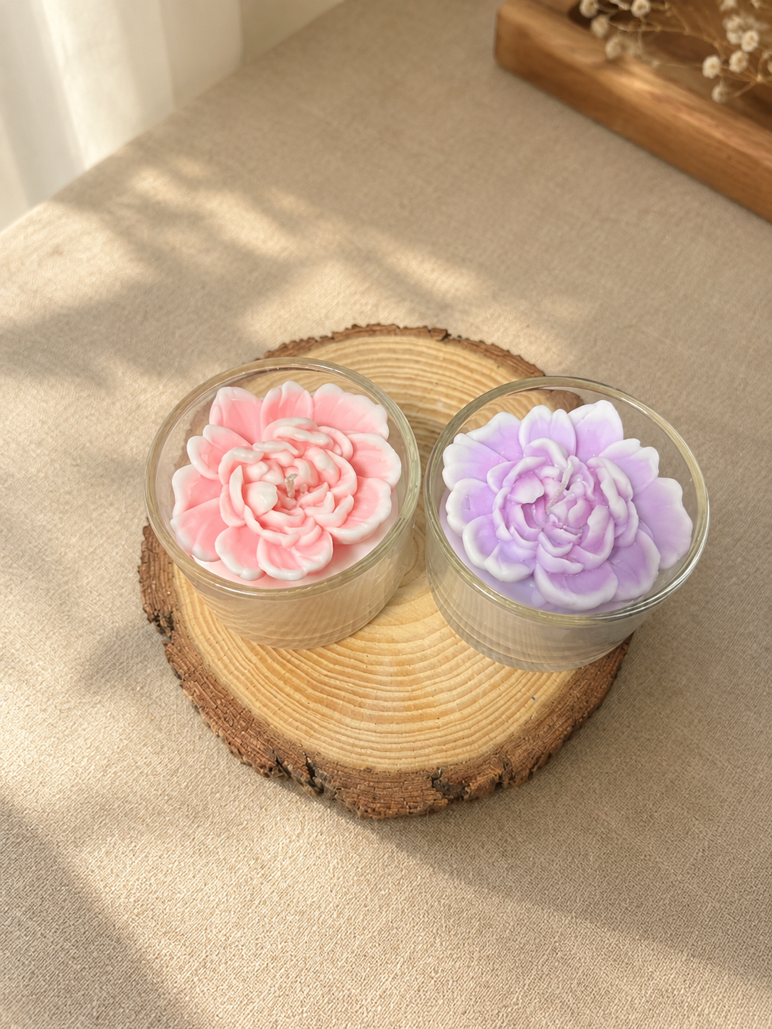 Pink and lilac peony candles in clear glass on a wooden slice