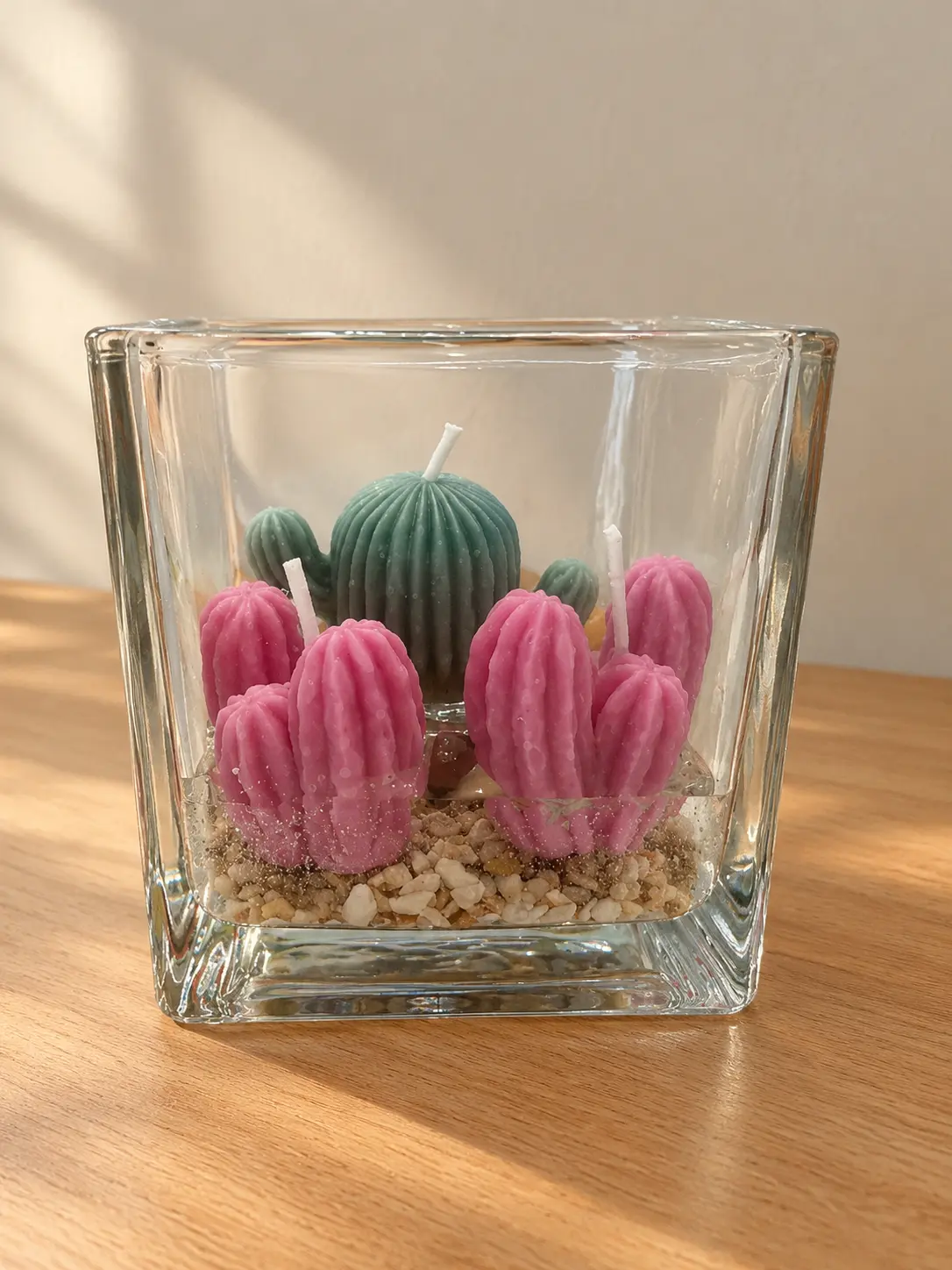 Square glass holder with pink and green cactus candles on small pebbles