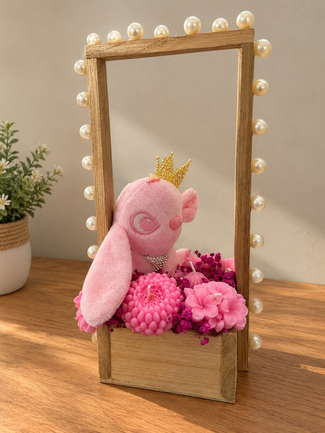Wooden pearl-trimmed carrier with a pink plush bunny wearing a gold crown among pink wax flower candles